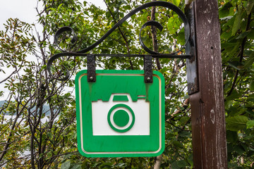 grünes hinweisschild mit kamerasymbol an holzmasten hängend