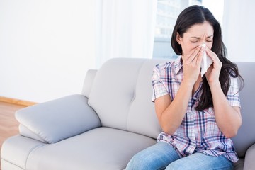 Pretty brunette sneezing on tissue on couch