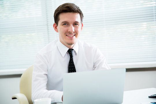 Handsome young businessman working at laptop in office.