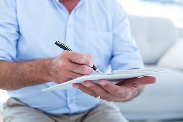 Businessman writing on notepad while sitting on sofa