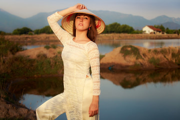 girl in Vietnamese hat against lakes rocks reflection