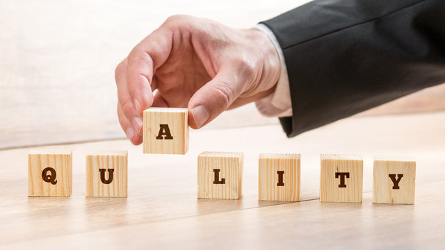 Businessman assembling the word Quality with seven wooden cubes