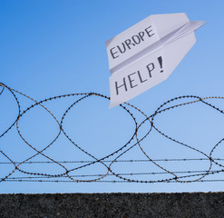 Papierflieger mit Aufschrift – EUROPE HELP! - fliegt über Absperrung aus Stacheldraht