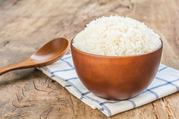 Cooked rice in bowl with spoon and dishcloth on old wooden table