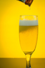 pouring beer to a glass on yellow backlight background, selective focused
