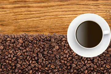 Close-up of roasted coffee beans and coffee cup over wooden back