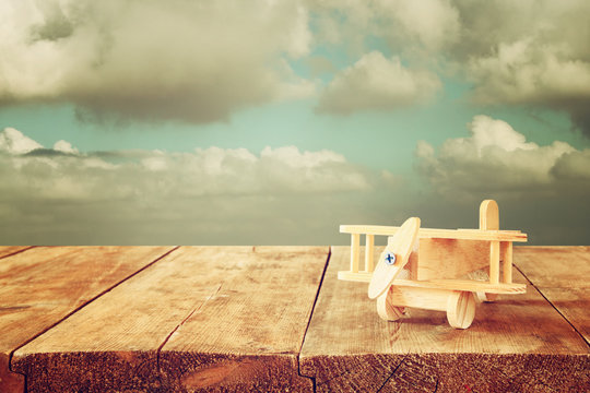image of wooden toy airplane over wooden table against cloudy sky. retro style image
