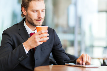     Handsome businessman enjoying a cup of coffee and looking his tablet