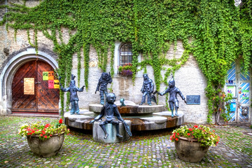 Ein wunderschöner Vorplatz in Lindau am Bodensee im Süden Deutschlands mit Statuen, einem Brunnen und einem alten Haus mit grünem Efeu - obrazy, fototapety, plakaty