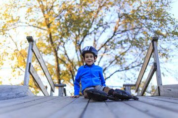 relaxation after roller skating. happy tired boy sitting on a wooden bridge resting after rollerblading