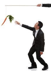 Tired businessman reaching for carrot on the end of a stick