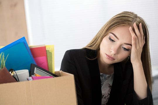 Young dismissed female worker in office sitting near carton box