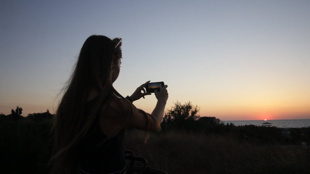 girl taking a picture with phone at sunset