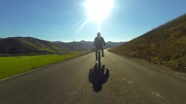 A man rides a motorized bicycle through the countryside on a two lane road.