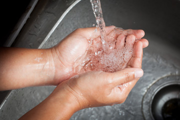 Fototapeta premium Woman washing her hands under running water in kitchen room
