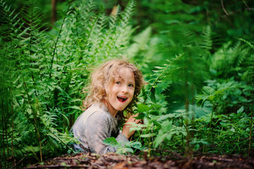 happy child girl hiding in wild ferns in summer forest