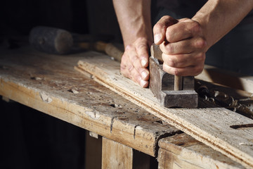 carpenter planing a plank of wood with a hand plane