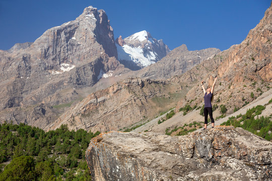Young Woman Staying on Rock with Arms Raised Up Female body on top of Stone Stretching body Towards Sun morning mountain landscape background