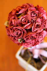 Artificial roses bouquet in small pot on wooden table.