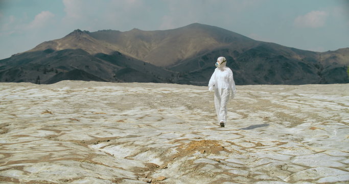 Researcher in protective coveralls and mask walking in arid radioactive area 