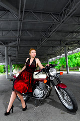 Naklejka na ściany i meble Biker girl in dress on a motorcycle over the background of dark