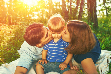 Fototapeta premium Happy parents kissing their child outdoors