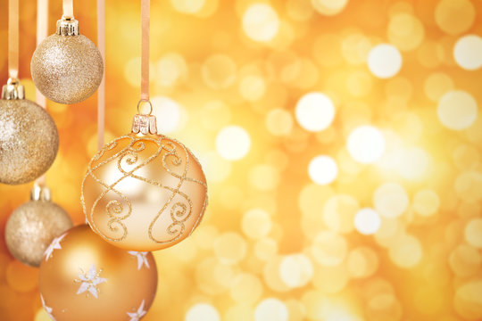 Gold Christmas baubles hanging in front of a gold background