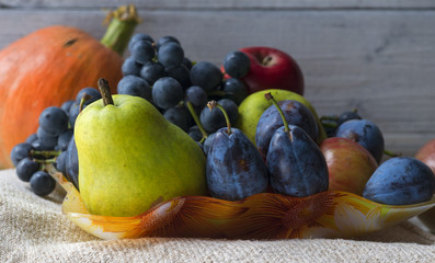Basket full of autumn fruits and orange pumpkin. Pear, apple, grape and plum