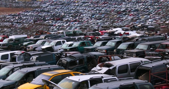 Cars sit in rows in a junkyard in the snow.