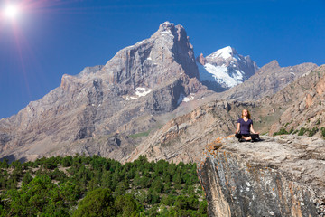 Fototapeta premium Young woman doing exercise Female Athlete Sitting in Yoga Zen Mediation Pose Mountain Panoramic Landscape Outdoor Orange Rocks Green Forest Clear Blue Sky High Summit Shining Sun