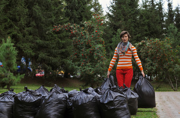 Woman gathering garbage in the park in plastic bags