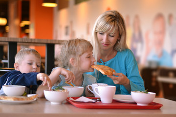 The young woman and two children eat in cafe

