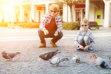 Two boys feeding doves on city square