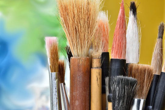 Close up of artists paint brushes. Mostly Chinese brushes standing vertically with a cheerful, colourful background.