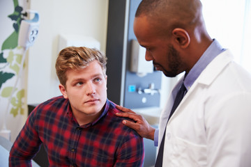 Male Patient Being Reassured By Doctor In Hospital Room