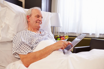 Senior Male Patient Using Digital Tablet In Hospital Bed