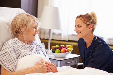 Obraz na płótnie Canvas Nurse Talking To Senior Female Patient In Hospital Bed