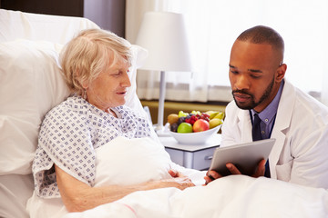 Obraz na płótnie Canvas Doctor Talking To Senior Female Patient In Hospital Bed