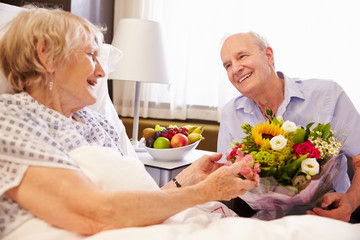 Obraz na płótnie Canvas Husband Visiting Senior Wife In Hospital With Flowers