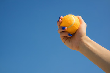 Female hand holds a bright orange tennis ball on a background of