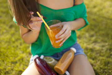 Girl holding a glass of juice in her hands. On the grass