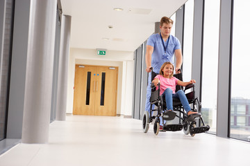 Nurse Pushing Girl In Wheelchair Along Corridor