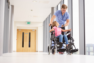 Nurse Pushing Girl In Wheelchair Along Corridor