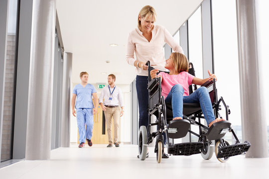 Mother Pushing Daughter In Wheelchair Along Corridor