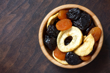 Wooden bowl of mixed dried fruit isolated on dark wood. From abo