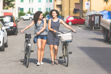 Female friends holding bikes and walking in the city