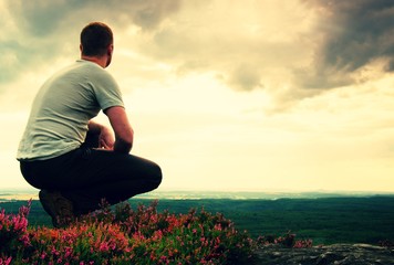 Hiker in squatting position on a rock in heather bushes, enjoy the cloudy scenery