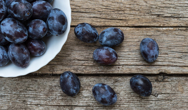 Plate full of fresh plums on a wooden background