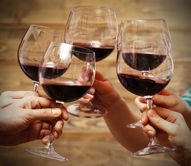 Clinking glasses of red wine in hands on rustic wooden planks background
