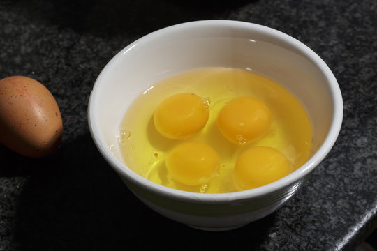 Several yolks and white egg into a ceramic bowl beside a brown egg